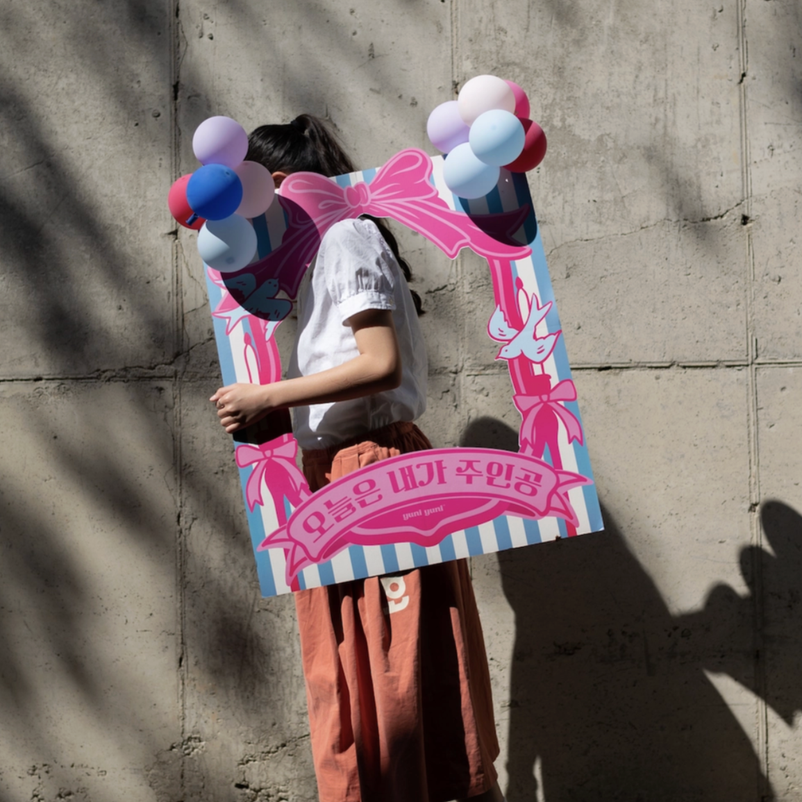 Person holding a large pink letter 'M' with balloons against a concrete wall.
photo frame, celebration deco, it's my day.