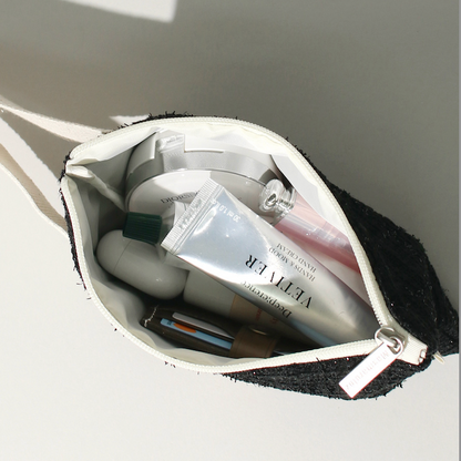 Open white makeup bag with cosmetic items on a light gray background