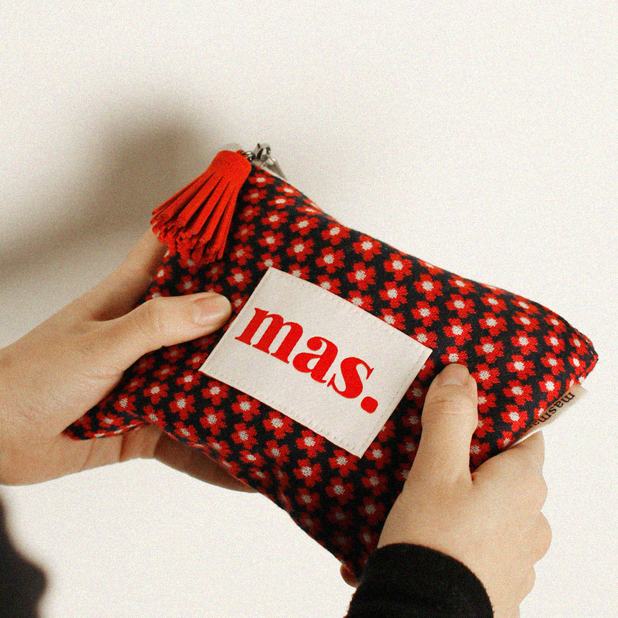 Red and black checkered pouch with 'mas' label held by a person against a white background