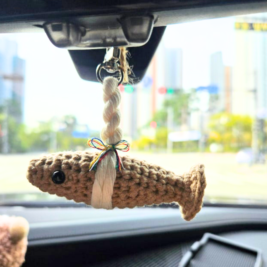 Car interior with a crocheted fish-shaped ornament hanging from the rearview mirror.