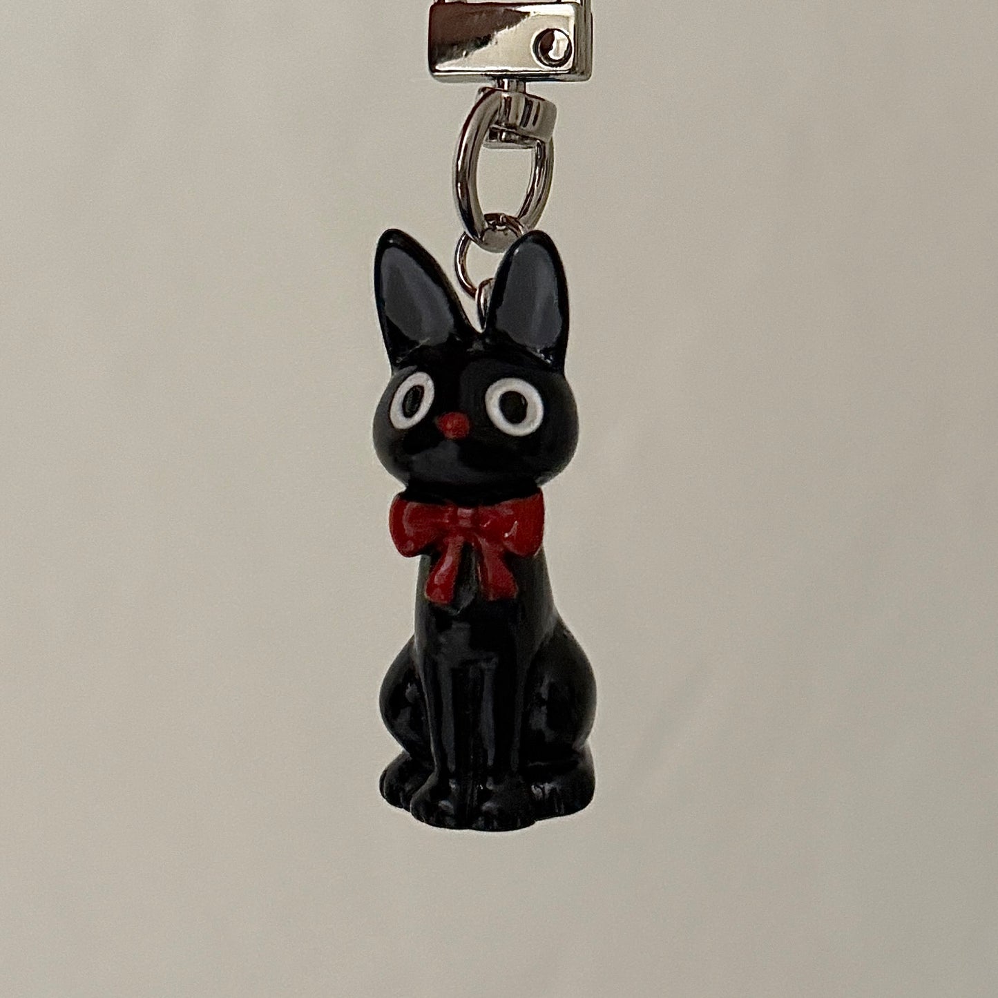 Black cat charm with a red bow on a gray background