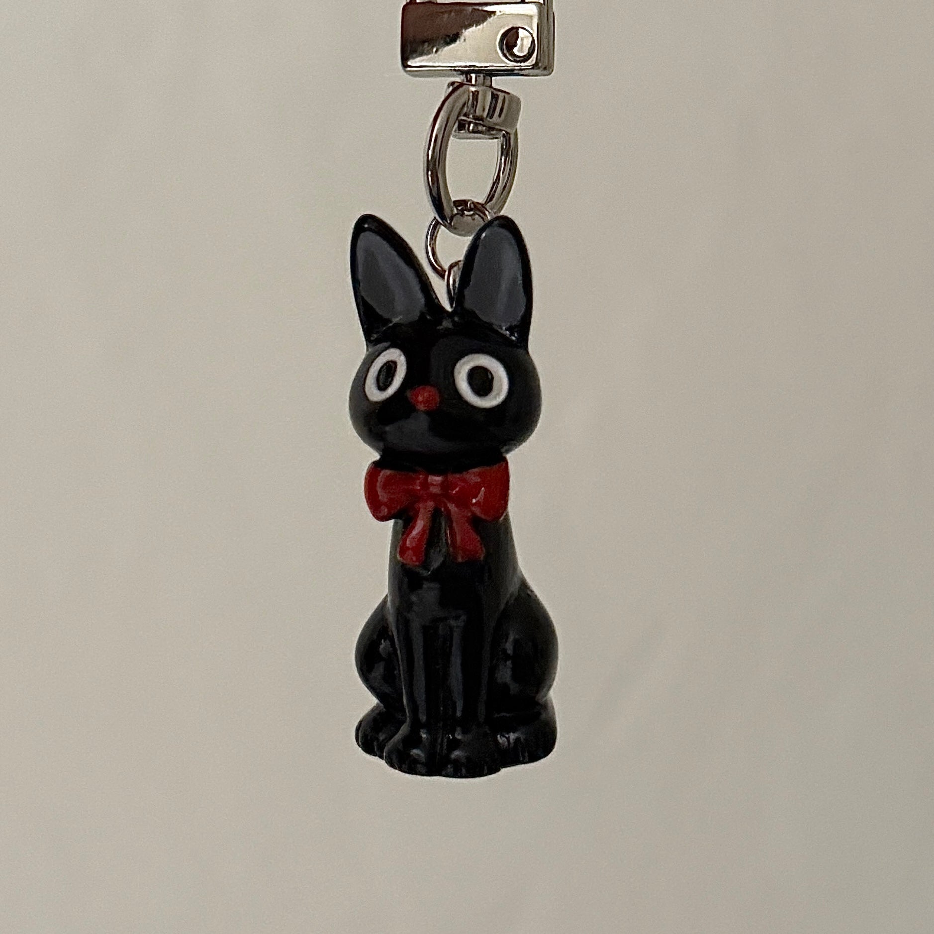 Black cat charm with a red bow on a gray background