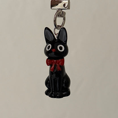 Black cat charm with a red bow on a gray background