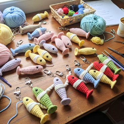 Colorful crocheted fish keychains on a wooden table with yarn and tools.