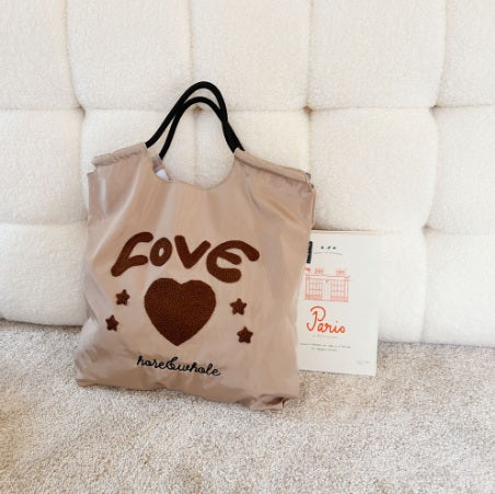 Beige tote bag with 'LOVE' and heart design on a textured surface