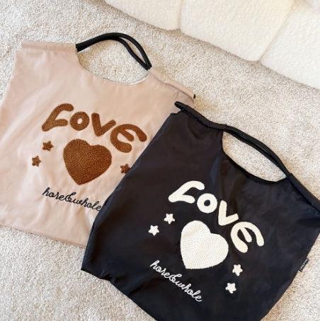 Two tote bags with 'love' and heart designs on a beige surface.
