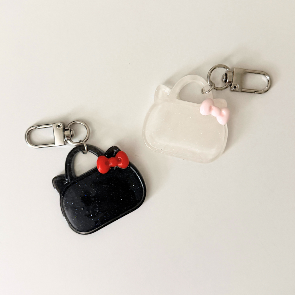 Two keychains shaped like black handbags with red bows on a light gray background