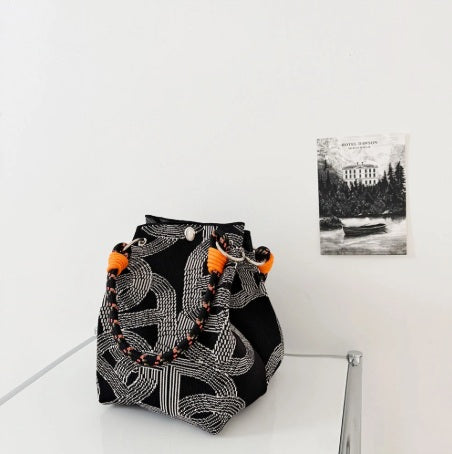 Black and white patterned bag with orange tassels on a white surface.