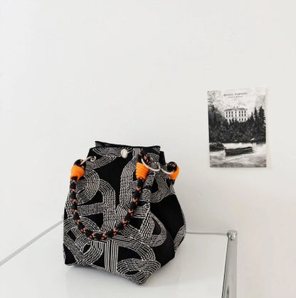 Black and white patterned bag with orange tassels on a white surface.
