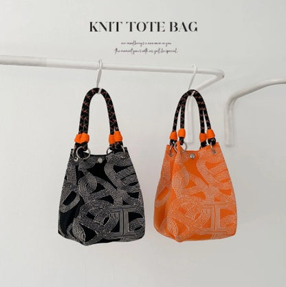 Two knit tote bags, one black and one orange, with patterns hanging on a rack.