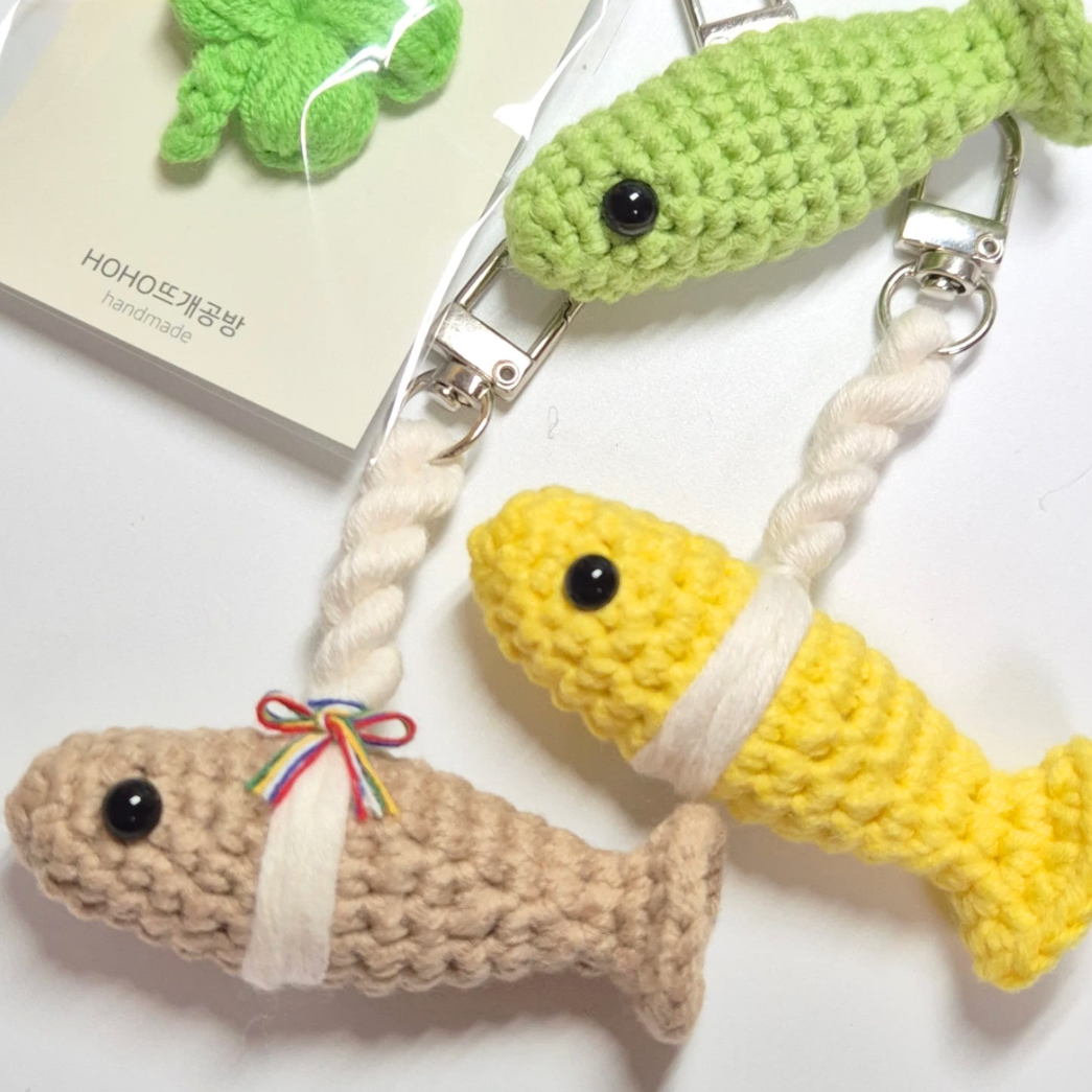 Three crocheted fish keychains in green, yellow, and brown on a white background.