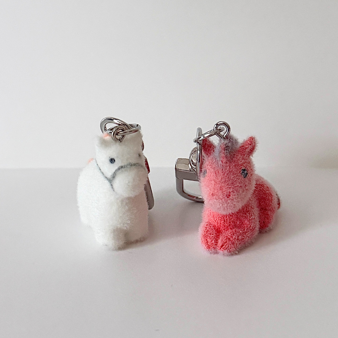 Two plush keychains, one white and one pink, on a light gray background.