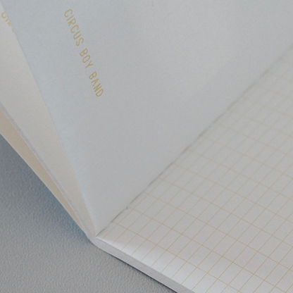 Notebook with grid paper on a gray surface, featuring 'Circus Boy Band' branding.