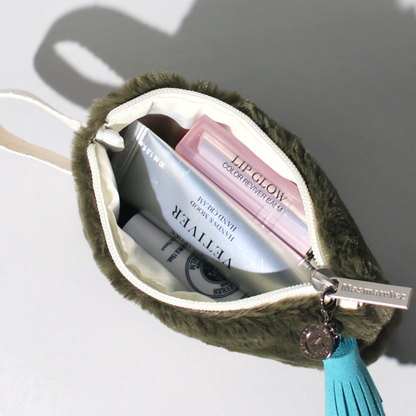 Open green pouch with cosmetic products and a blue tassel on a white background