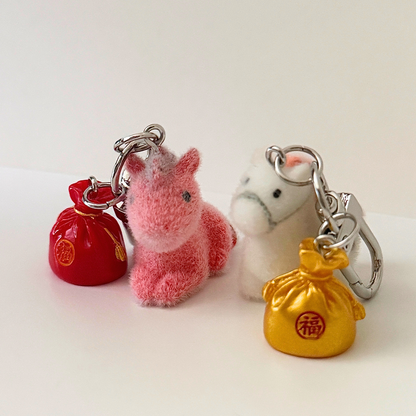 Set of keychains including a red bag, pink plush animal, and gold bag on a white background